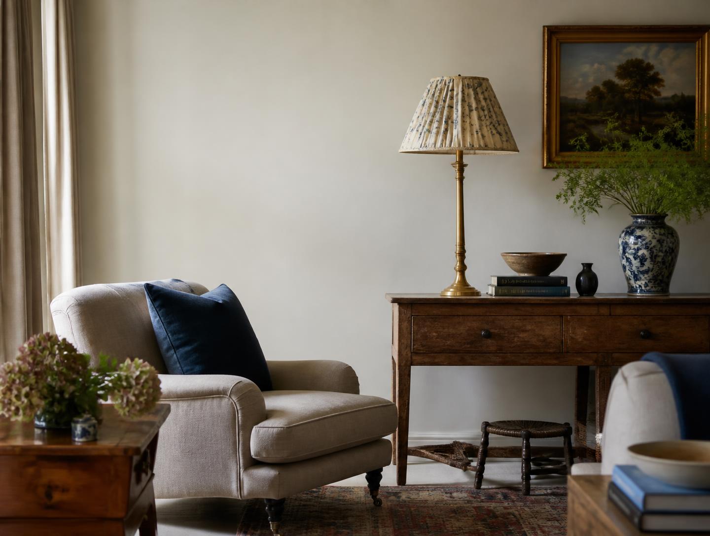 A calm English sitting room with aged wood, linen and a pleated brass lamp